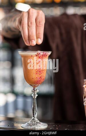 Barman professionnel décoré orange cocktail alcoolique avec rose rouge. Vue floue Banque D'Images