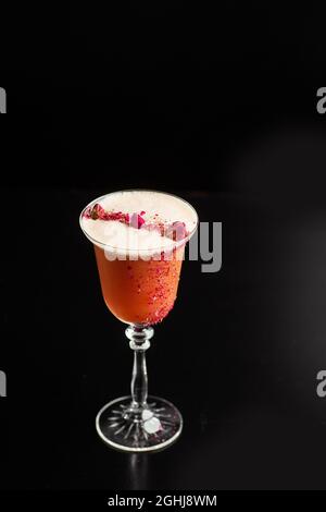 Verre avec cocktail d'orange décoré de roses séchées sur le bar sur fond noir. Les boissons sont décorées de fleurs. Banque D'Images