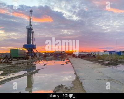 Un champ de pétrole avec une plate-forme de forage et des wagons. Réflexion dans une flaque au coucher du soleil. Industrie pétrolière. Banque D'Images