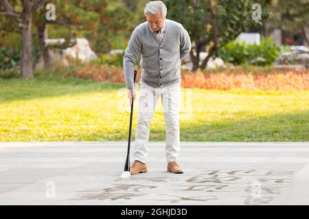 Homme senior pratiquant la calligraphie dans le parc Banque D'Images