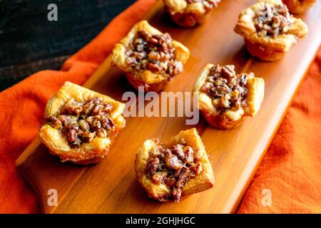 Tartelettes de pacanes servies sur une planche à découper en bois : tartes individuelles de pacanes exposées sur une planche à découper en bois Banque D'Images