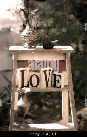 Les mots d'amour recueillis avec des vases vintage et un oiseau sur une échelle dans le jardin Banque D'Images