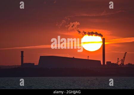 Vue en téléobjectif d'un coucher de soleil orange épique sur le port de Dublin et le soleil en alignement avec l'usine de Covanta (Dublin Waste to Energy) vue depuis l'embarcadère ouest de Dun Laoghaire Banque D'Images