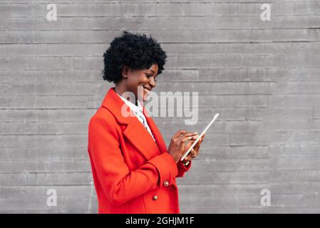 Femme afro-américaine élégante souriante en utilisant une tablette numérique en plein air dans la rue. Banque D'Images