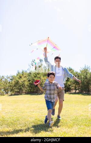 Un père et un fils heureux qui s'exécutent avec du cerf-volant dans la prairie Banque D'Images