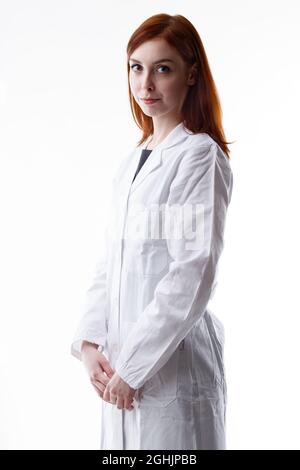 Jeune femme sérieuse technicien, médecin, ambulancier ou infirmière dans un manteau blanc de laboratoire debout sur le côté regardant la caméra avec une attention sérieuse expres Banque D'Images