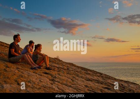 amis deux femmes et un homme au coucher du soleil s'assoient sur une montagne au-dessus de la mer et regardent au loin Banque D'Images
