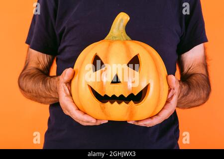 Détail d'une terrifiante citrouille « Jack-o-lanterne » tenue par les mains sur fond orange. Halloween et le concept des jours morts. Banque D'Images