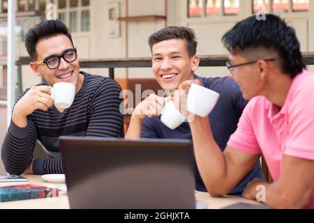 Trois jeunes étudiants boivent du café à l'extérieur tout en parlant et en riant. Banque D'Images