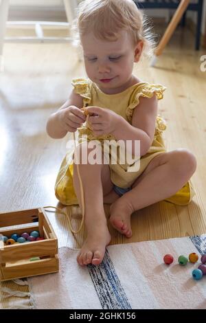 Fille souriante jouant des perles amovibles en bois pour le développement de fines compétences de moteur Maria Montessori matériaux Banque D'Images