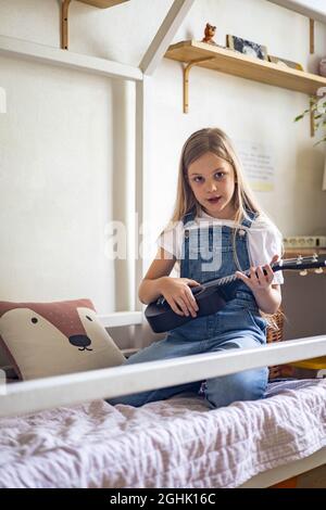 Focalisé petite fille jouant la mélodie sur ukulele pratiquant l'exercice musical appréciant l'étude éducative Banque D'Images