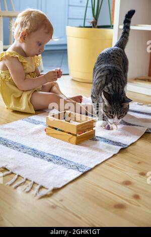 mignon bébé fille en robe ayant amusant couché sur le sol avec chat jouant des perles amovibles en bois Banque D'Images