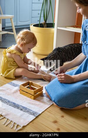 Bonne famille mère, fille et chat passer du temps ensemble à jouer des matériaux Maria Montessori Banque D'Images