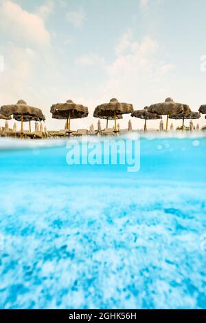 (Mise au point sélective) prise de vue fractionnée, au-dessus de la photo. Eau turquoise cristalline et quelques parasols de plage illuminés au cours d'un lever de soleil époustouflant. Banque D'Images