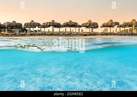 (Mise au point sélective) prise de vue fractionnée, au-dessus de la photo. Eau turquoise cristalline et quelques parasols de plage illuminés au cours d'un lever de soleil époustouflant. Banque D'Images