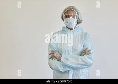 Infirmière sérieuse en costume d'EPI, masque médical et gants, croisant les bras et regardant la caméra, isolée de blanc Banque D'Images