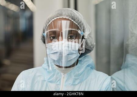 Visage d'une infirmière médicale noire fatiguée en costume d'EPI, masque médical et écran facial protégeant du coronavirus Banque D'Images