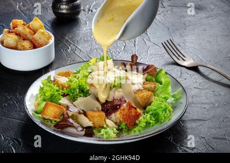 Salade César au poulet avec la vinaigrette classique versée, croûtons et poivre, sur fond noir Banque D'Images