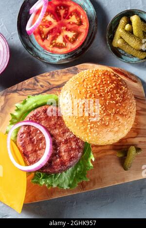 Recette de hamburger. Ingrédients classiques de hamburger à base de viande avec patty de bœuf, petits pains au sésame, tomate, oignon, feuille de salade et cornichons, tiré par le haut Banque D'Images