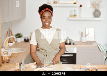 Une jeune femme de ménage africaine couchant de la pâte maison pour la pâtisserie sur une table de cuisine Banque D'Images