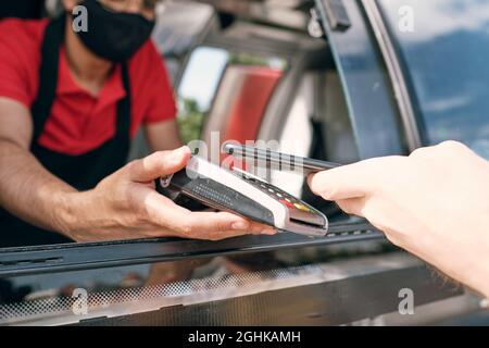 Vendeur de nourriture à emporter tenant le terminal de paiement dans la fenêtre du camion pendant que le client paie pour la collation Banque D'Images