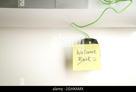 Bienvenue avec un smiley écrit sur un bâton de papier jaune sur la souris d'ordinateur sur le dessus de la table de bureau. Banque D'Images