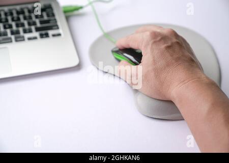 Main de l'homme cliquant sur la souris, reposant son poignet sur le repose-poignet ou soutenant la mousse à mémoire de forme. Gros plan. Banque D'Images