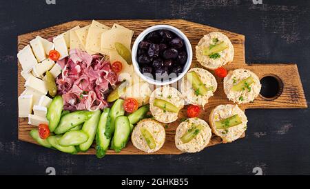 Plateau de restauration antipasti avec jamon, fromage, canape et olives noires sur une planche en bois. Vue de dessus, au-dessus de la tête Banque D'Images
