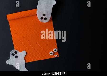 Mackeup Halloween. Une feuille orange vide sur un arrière-plan noir et des fantômes blancs. Joyeux Halloween, espace pour le texte Banque D'Images