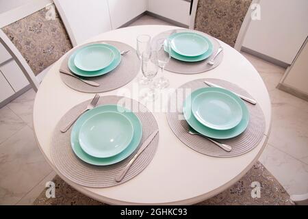 Table de cuisine avec assiettes et verres turquoise. Couverts sur table blanche, intérieur Banque D'Images