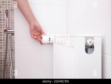 la femme allume le radiateur de chauffage dans la salle de bains avec un thermostat. Réglage d'une température confortable dans la salle de bains Banque D'Images