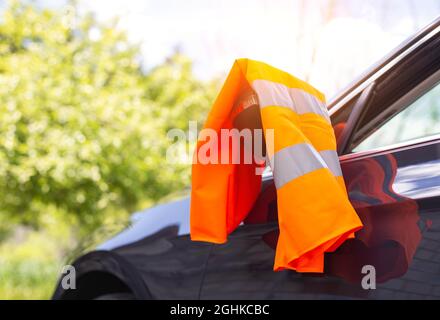 Un gilet d'avertissement orange est suspendu sur le rétroviseur d'une voiture de tourisme. Concept de panne de voiture, signal d'assistance routière, problèmes Banque D'Images