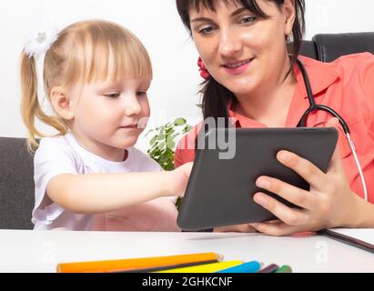 Une femme médecin, pédiatre, présente un dessin animé d'une jeune fille de 3-4 ans sur une tablette. Une approche individuelle du traitement de chaque enfant Banque D'Images