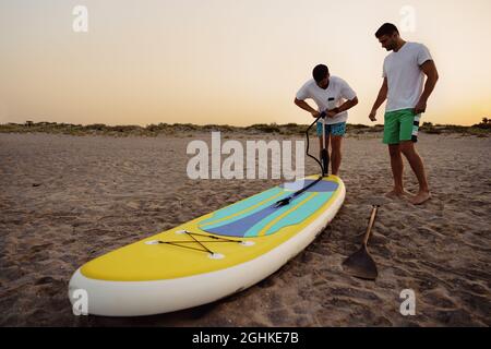 Jeune homme gonflant paddle sup bord sur la plage au lever du soleil Banque D'Images