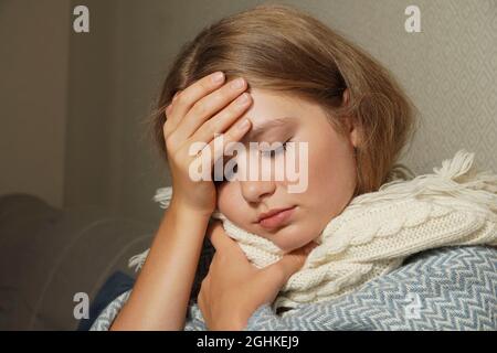 La femme éternue dans un mouchoir blanc. Jeune femme blonde enveloppée dans une couverture chaude, éternuant, a la grippe. Banque D'Images