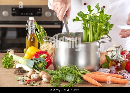 Chef préparant des ingrédients frais et sains de légumes pour la soupe ou le hot pot dans une casserole tenant une louche en acier inoxydable au-dessus de la casserole dans un gros plan sur le Banque D'Images