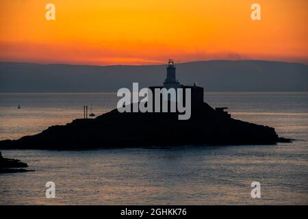 Swansea, Royaume-Uni. 07septembre 2021. Un petit bateau à voile se fait passer devant le phare éclairé de Mumbles près de Swansea, tandis que la brume de mer commence à se dégager au lever du soleil tôt ce matin au début d'une superbe journée d'automne. Credit: Phil Rees/Alamy Live News Banque D'Images