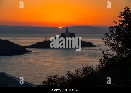 Swansea, Royaume-Uni. 07septembre 2021. Un petit bateau à voile se fait passer devant le phare éclairé de Mumbles près de Swansea, tandis que la brume de mer commence à se dégager au lever du soleil tôt ce matin au début d'une superbe journée d'automne. Credit: Phil Rees/Alamy Live News Banque D'Images