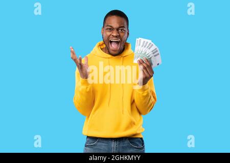 Un homme noir émotif criant tenant l'euro sur fond bleu Banque D'Images