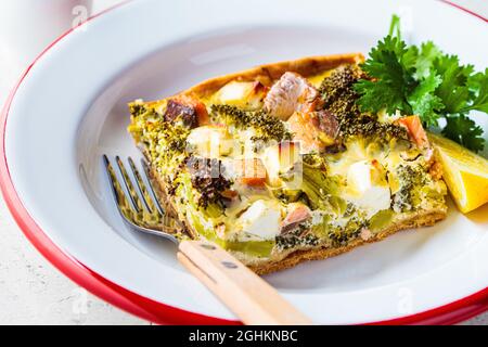 Morceau de tarte à la quiche avec saumon et brocoli dans un plat, gros plan. Banque D'Images