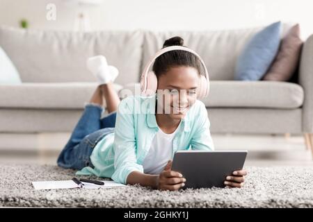 Petite fille étudiant en ligne en utilisant l'appareil à la maison. Belle jeune fille avec micro-casque d'apprentissage à distance pendant Covid-19 Banque D'Images