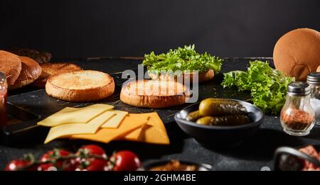 Bannière Panorama présentant les ingrédients d'un hamburger de bœuf gastronomique avec petits pains grillés, ingrédients de salade, cornichons, fromage, tomate et condiments sur un kit Banque D'Images