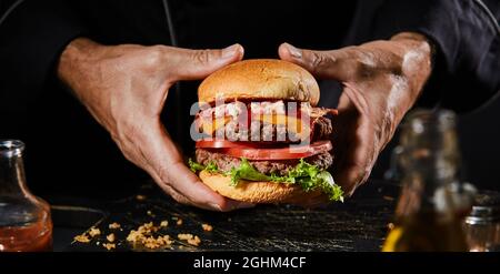 Bannière Panorama avec les mains d'un homme tenant un double hamburger de bœuf, whopper ou Big Boy avec du bacon, de la salade et des garnitures de fromage sur un pain grillé pour le menu Banque D'Images