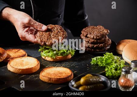 Le chef prépare des hamburgers avec des viandes grillées faites maison en plaçant un sur un petit pain avec de la laitue verte fraîche en gros plan sur la main Banque D'Images