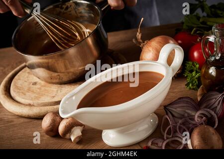 Bateau à sauce rempli de sauce épicée brune, vue en grand angle sur une table de cuisine avec divers ingrédients de légumes frais Banque D'Images