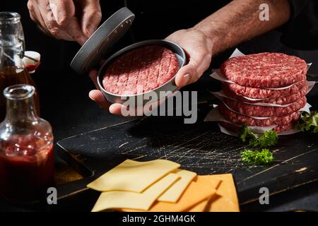 Chef préparant des patties de bœuf maison à l'aide d'un presse-patty ou d'une presse à hamburger en gros plan sur la viande et l'ustensile dans ses mains Banque D'Images