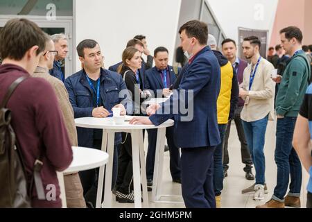 Moscou - 26 avril 2021: Groupe d'entrepreneurs masculins en vêtements décontractés avec des badges discutant de questions d'affaires tout en ayant une pause café pendant le séminaire Banque D'Images