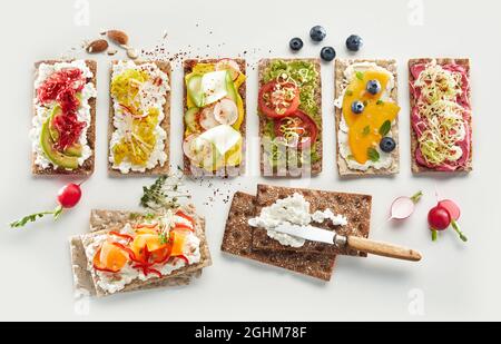 Vue de dessus de l'arrangement des toasts de pain croustillant avec des fruits frais et des légumes assortis placés sur fond blanc pour les repas végétariens santé Banque D'Images