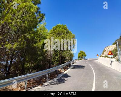 Route escarpée de montagne avec panneaux d'avertissement de la plage de galets de Gialos avec ciel bleu clair, île de Lefkada, Grèce. Soleil été pittoresque da Banque D'Images