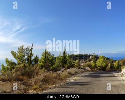 Route de montagne près du village de Kalamitsi avec ciel bleu clair, île de Lefkada, côte de mer Ionienne, Grèce. Excursion pittoresque d'une journée ensoleillée en été avec long sha Banque D'Images